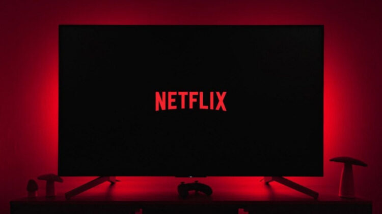 Kırmızı loş ışıkta bir televizyon ve televizyon ekranında Netflix logosu